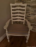 Front view of one painted white wooden chair with ladder-back and patterned cushioned seat, showing turned legs and armrests, positioned on hardwood floor.