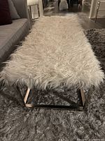 Front angle view of rectangular faux fur upholstered bench with metal base on gray shag rug.