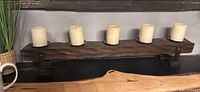 Dark wooden wall-mounted candle holder with metal brackets supporting five ivory pillar candles arranged in a row.