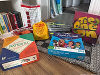 Photo of multiple boxed board games including Personal Preference, Trivial Pursuit (two boxes), Tie One On, and a yellow sealed packet game