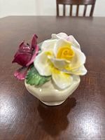 Front angle of porcelain floral figurine showing white and yellow rose with green leaves on a cream base