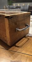 Close-up side view of the wooden box showing natural wood texture and metal handle.