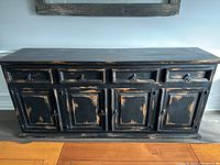 Front view of distressed black wooden hutch showing four drawers and four doors