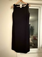 Sleeveless black dress hanging on a hanger showing front view