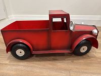 Side view of red metal planter shaped like a vintage truck, showing detailed black and white tires and a headlight on the front.