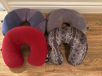 Four U-shaped neck protectors in different colors and patterns lying on a wooden floor.
