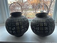 Two black metal lanterns with floral cutout pattern, hanging handles visible