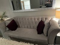 Front view of entire sofa showing tufted back, rolled arms, and two dark red throw pillows