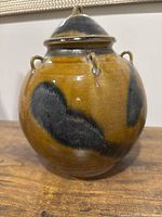 Side view of the vintage yellow-brown glazed ceramic jar showing black abstract patterns and loop handles, placed on wooden surface.
