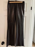 Full view of the vintage Danier black leather pants hanging on a hanger, showing the straight leg style and leather texture.