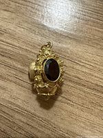 Vintage gold pendant photographed on a wood surface showing front and angled views, highlighting the three large faceted garnet stones and ornate gold detail.