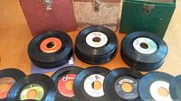 Photo showing stacks of 45 RPM vinyl records along with three vintage-style storage boxes in green, beige, and red with metal clasps.