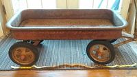 Side view of the antique Radio Flyer wagon showing rusty red metal body and four metal spoked wheels.