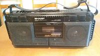 Front view of Sharp double cassette boom box showing speakers, cassette deck, and carrying strap.