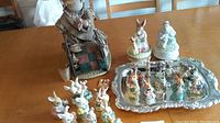 Photo showing vintage collectible bunny figurines including a large one in a rocker chair, small white bunnies, and a silver tray with multiple figurines displayed.