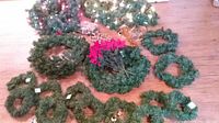 Photo showing assorted artificial Christmas wreaths including large, medium, and small sizes with some decorations like red flowers.