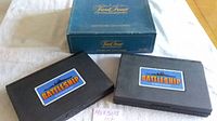 Three game boxes shown, one blue box for Trivial Pursuit Master Genus Edition and two black plastic cases labeled Battleship.