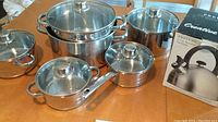 Overview of five stainless steel pots and pans with glass lids.