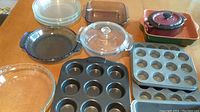 Overview of the entire set showing multiple Pyrex glass pie plates and casserole dishes, metal muffin pans, and ceramic casserole.