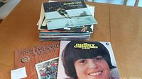 Stack of 24 vinyl record albums on a wooden table with visible album covers of Bobby Orr hockey album, The Osmonds Homemade, and Donny Osmond album