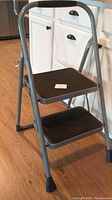Front angle view of the 2 step stool ladder showing both steps, metal frame, and black textured treads.