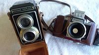 Front view of Kodak Reflex twin lens reflex camera alongside Praktica FX3 camera, showing camera bodies and attached leather cases