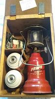 Top-down view inside wooden box showing copper-red Prepo Light Model 400 lantern, two fuel cans, green mantle package, and small box.
