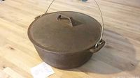 Side angle showing the Dutch oven with lid and bail handle on a wooden surface with a note.