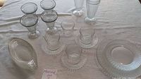 Full lot showing various vintage glass dessert cups, small plates, saucers, and a carafe on white tablecloth