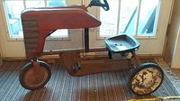 Side view of a vintage red metal pedal tractor with a single front rubber tire and two rear metal wheels with chipped paint.
