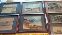 Seven framed watercolor prints arranged together on a floor showing coastal and harbor scenes