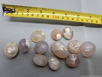 Twelve flower agate tumble stones arranged on white surface next to measuring tape for size reference.