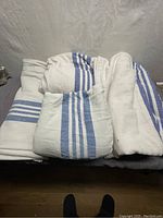 Four folded vintage hospital blankets with blue stripe pattern stacked on surface. Blankets show signs of wear and dirt.