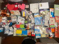 Numerous assorted craft supplies laid out on a dark table, featuring heart cutouts, ribbons, and packaged small craft accessories.