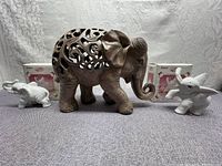 All three elephant figurines shown together: one large carved brown figurine, two smaller white porcelain figurines with one in box