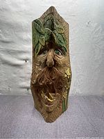 Front view of hand carved wood log sculpture with face, leaves, and bird motif.