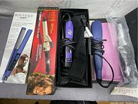 Top-down view of four hair styling tools including two boxed and two unboxed items, cords coiled, one protective pouch