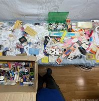 Wide view of the lot showing assorted pins, buttons, threads, sewing tools and notions spread out on a surface.