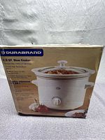 Front and side views of the boxed Durabrand 2.0 quart slow cooker showing product image, text in English and French highlighting features such as removable stoneware, temperature settings, and compact size.