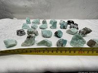 Raw amazonite stones laid out in two rows on a white cloth with a measuring tape in front showing sizes approximately 3-7 cm.
