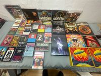 Wide shot of 33 rock and classic rock cassette tapes, CDs and DVDs laid out on a table, showing the variety of albums and artists in the lot.