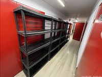 Long hallway view showing five black shelving units side by side against red and corrugated walls