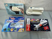 Lot overview showing Steamette steamer with original box, Handystitch handheld sewing machine in box, SwiftShear fabric cutters in box, and loose luggage fabric lint remover.
