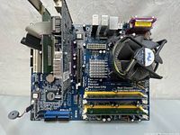 Full top view of blue computer motherboard with Intel CPU cooler and various slots and connectors.