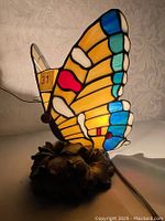 Front view of the lit butterfly stained glass lamp showing vibrant colors and floral base.