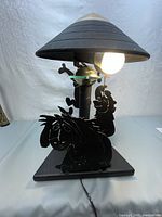 Photo showing front view of black metal lamp with a conical shade and Winnie the Pooh character silhouettes including Pooh and Eeyore in front, lit with bulb on.