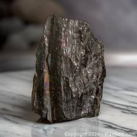 Front angled view of black Tourmaline rod with visible natural striations and shiny black surface with some iridescence.