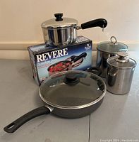 Revere Ware 2 qt covered saucepan on original box, 2 steel canisters with lids, one marked Fabrique En Coree 1.5 quart, the other unmarked stainless steel, and an 11 inch Domo pan with glass lid and black handle