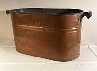 Side view of the oval copper wash tub showing wear and dents.