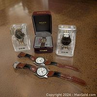 Five men's watches: two Kmart black metal band watches, two leather strap watches with white faces, and one Gruen watch in an open maroon box